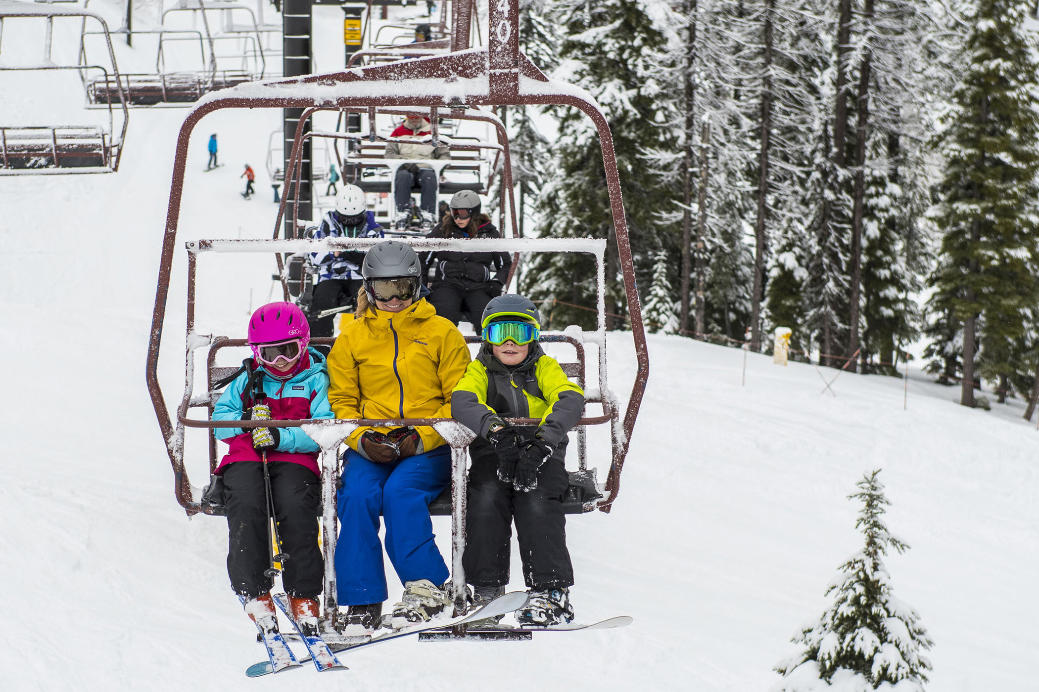 Kids and families riding a chairlift above snow‑covered trees at an Idaho ski resort, representing the winter experiences included in the Ski Idaho 5th and 6th Grade Passport.